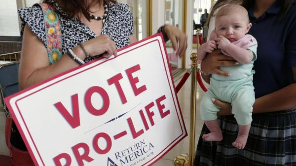 An anti-abortion supporter from Moore County holds a sign next to a 3-month-old baby as they wait to enter the Senate gallery, Tuesday, May 16, 2023, in Raleigh, N.C., as state legislators debate on whether to override Democratic Gov. Roy Cooper's veto of a bill that would change the state's ban on nearly all abortions from those after 20 weeks of pregnancy to those after 12 weeks of pregnancy. Both the Senate and House had to complete successful override votes for the measure to be enacted into law. (AP Photo/Chris Seward)