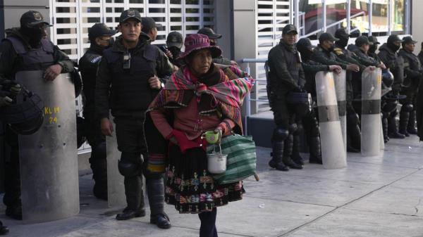 A woman walks past police officers standing guard the Financial Regulatory Authority offices, in La Paz, Bolivia, Wednesday, May 31, 2023. A prosecutor in Bolivia launched an investigation Mo<em></em>nday into the mysterious death of the trustee of a bankrupt bank who fell from the 15th floor of a building and his family disputed claims he took his own life. (AP Photo/Juan Karita).